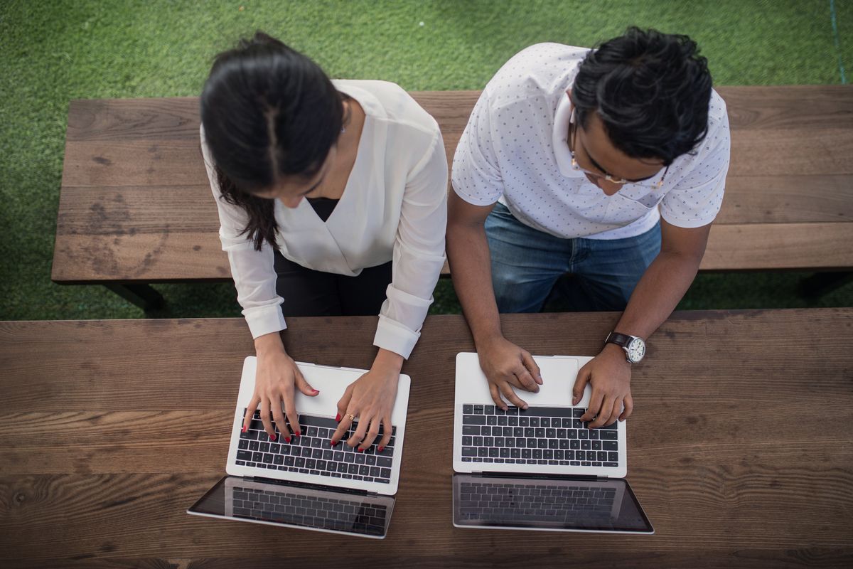 Two people on laptops sitting side by side at a table