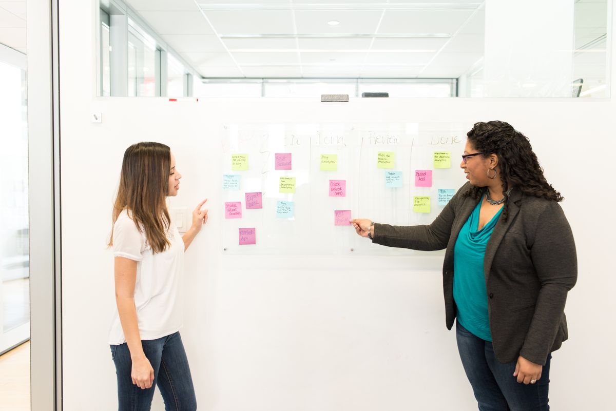 Two women using post-it notes on a whiteboard to collaborate