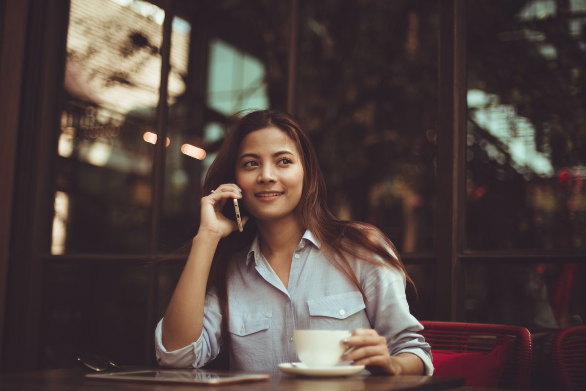 Photo of a woman drinking coffee outside while taking on the phone